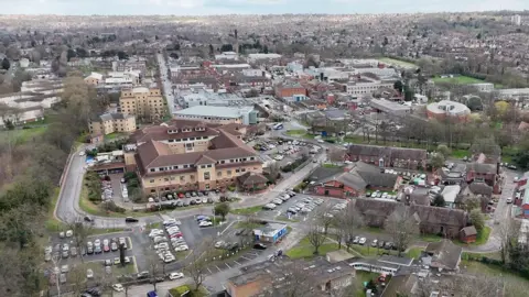 A drone-image of Nottingham City Hospital with city skyline in the background. Car parks and surrounding buildings can be seen in the aerial image
