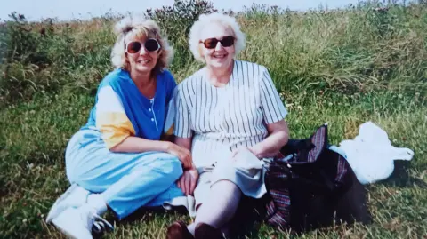 Judith Gaughy Judith and her mum siting on the grass in summer both smiling at the camera 
