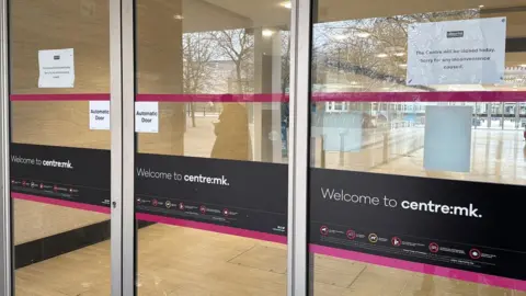 Richard Knights/BBC The glass doors to the shopping centre are closed and there are white A4 signs in the window that read: "The Centre will be closed today. Sorry for any inconvenience caused"
