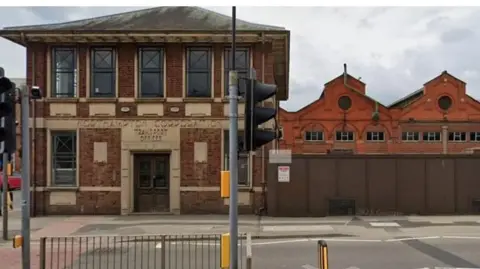 Google A red bricked two-storey building with the words Northampton Corporation Transport Offices above the door. It stands on the corner of a road in front of a pedestrian crossing.