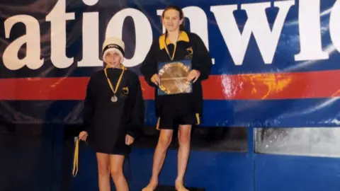 Jazz Carlin An old photo of two young people wearing medals and smiling while wearing jumpers which say 'tigersharks.'