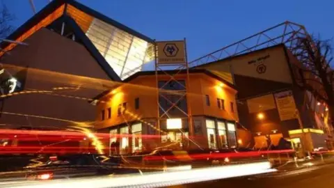 The outside of Molyneux stadium. Its dark but the lights are yellow and red with lines swirling outside the yellow building