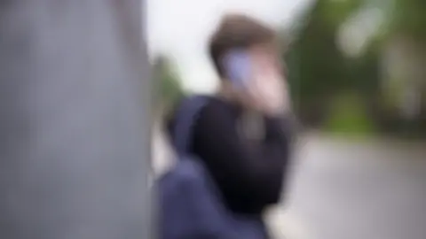 A blurred picture of a young man holding a phone to his ear.