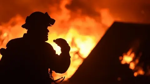 AFP A firefighter drinks water in front of a burning house near Oroville, California (09 July 2017)