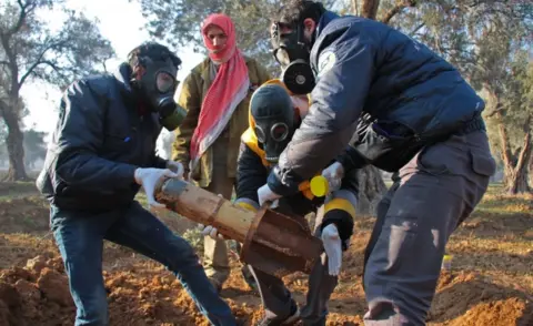 AFP/Getty Images Syria Civil Defence members in gas masks carefully handle remnants of a rocket