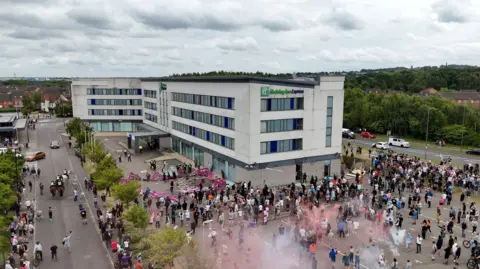 Reuters A drone view shows demonstrators protesting outside a hotel as police officers stand guard in Rotherham, Britain.