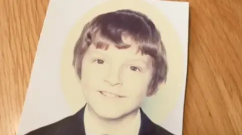 A boy with dark hair is wearing a dark jacket and white shirt.