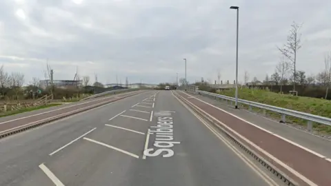 Squibbers way road in Bridgwater, where the road crosses the River Parrett. There is a white van in the background coming towards the camera and buildings on the left.