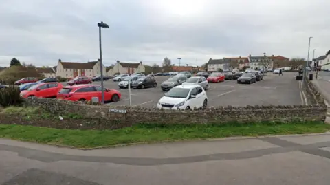 Google Rock Street car park in Thornbury. It is situated on a hill, on a bend in the road. It is surrounded by a brick wall and a footpath.