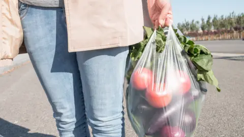 Getty Images A woman carrying a clear plastic bag containing vegetables. Only their hands, legs and the bag can be seen in the frame. 