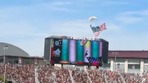 The skydiver begins his descent into the Virginia tech scoreboard.
