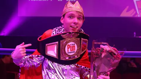 Adam Ernest Pickard bathed in purple light with a boxing-style belt around his shoulders