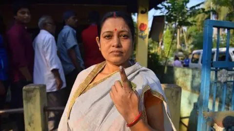 Getty Images Seorang pemilih menunjukkan jarinya yang bertinta setelah memberikan suara di tempat pemungutan suara pada pemungutan suara daerah pemilihan Majelis Samaguri di distrik Nagaon, Assam, India, pada 13 November 2024. 