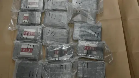 National Crime Agency Plastic boxes wrapped in plastic with 'prada' labels on them are laid out on brown paper