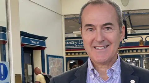 Clare Worden/BBC Mark Collins stands in the doorway at King's Lynn train station. He is wearing a navy suit and a purple striped shirt. He has short greying hair. 