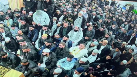 Oldbury Jamia Masjid A large gathering of men sat in a row looking towards the left of the photo