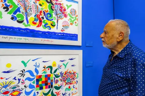 ANOUK RIONDET / AFP / GETTY IMAGES A man stands close to colourful paintings.