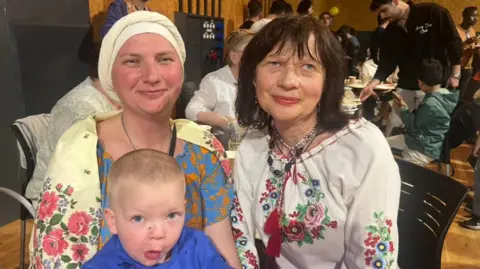 Two women wearing flowery clothes with young boy wearing blue.