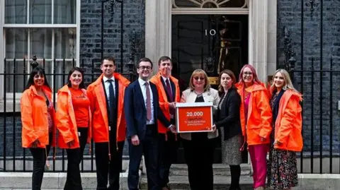 Coeliac UK Nine people stand in front of 10 Downing St with a sign about the petition