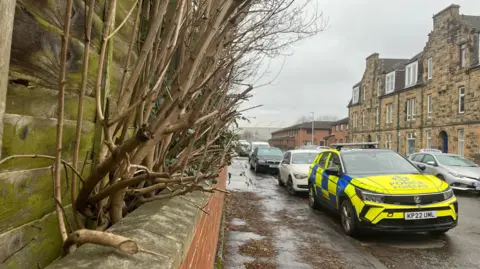 A marked blue and yellow Police Scotland car vehicle parked in front of other cars on a street