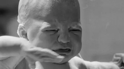 Ester moments after being born. The black and white photograph shows her being held by a medic. She is crying.