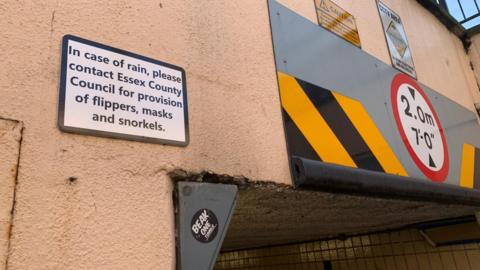 A sign above an underpass that reads: "In case of rain, please contact Essex County Council for provision of flippers, masks and snorkels."