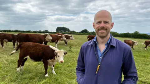 Farmer Jimmy Woodrow stands among a field of cows