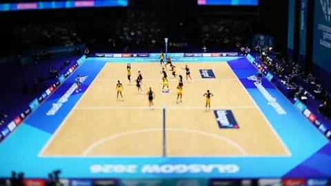 Getty Images A view looking down on a netball match at the Commonwealth Games, with players in yellow and black uniforms playing each other.