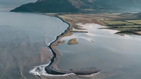 Photo provided by the South West Coast Path Association, Photographer: Marlena Ciach An aerial image overlooking a marsh area which has been engulfed by still waters. The water is flooding over fields in the background. 