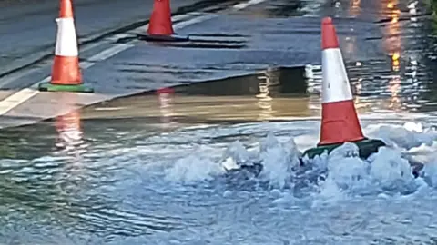 A road cone being lifted by the force of water emerging from a flooded road.