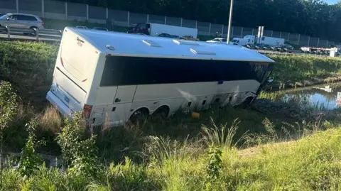 Virginia State Police A white and black bus sits on greenery on the side of a road after a crash.