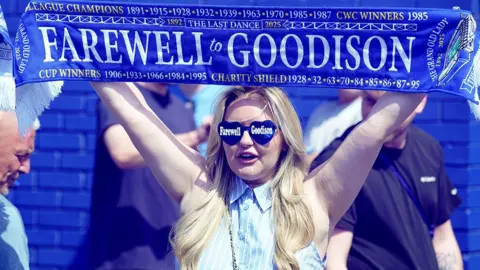 PA Media A female Everton fan with long blonde hair outside the ground holding a scarf in the air that says 'Farewell Goodison'