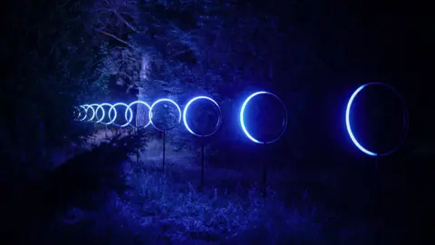 Hoops lit up with blue light on grass, stretching in a line into the distance.