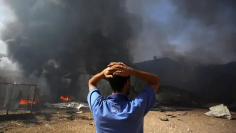 Reuters A man stands near a burning sponge factory after it was hit by Israeli artillery shells in Gaza