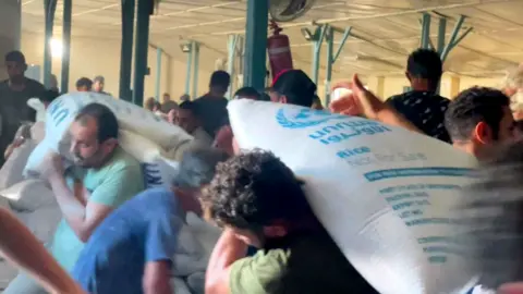 Displaced Palestinians carry food bags and boxes as they storm an UNRWA food supply centre in Deir el-Balah in the southern Gaza Strip after smashing doors on 28 October