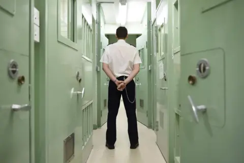 Michael Cooper A prison guard stands in the corridor of a prison with his back to the camera.