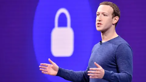 Getty Images Mark Zuckerberg gestures with arms open in front of a padlock symbol on stage during a privacy speech