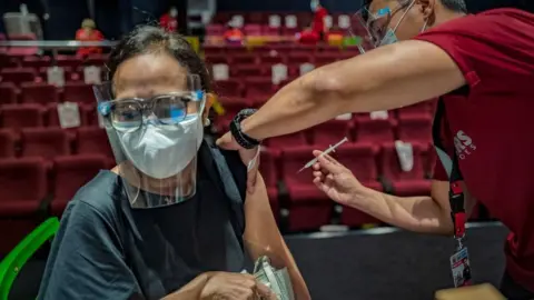 Getty Images A healthcare worker administers a dose of Sinovac Biotech's CoronaVac vaccine to a woman at a mall theatre converted into a vaccination centre on June 1, 2021 in San Juan, Metro Manila, Philippines