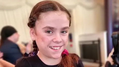 Lucy Watson Carmela Chillery-Watson looks at the camera. Her hair is tied back and she's in a marquee