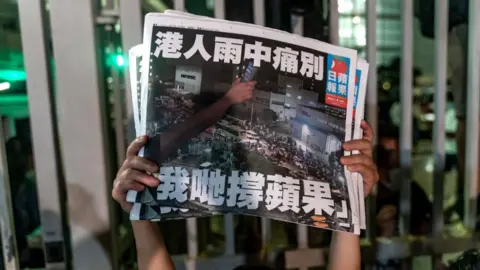 Getty Images An employee holds up the latest copies of the Apple Daily newspaper