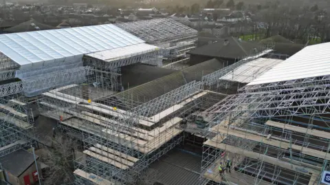 BBC The H-shaped hospital building is surrounded by scaffolding as well as a huge canopy over the far left, long stretch of the hospital, which allows work to be done in all weathers beneath it. The picture is taken from above the hospital by a drone and gives a sense of the scale of the work being done.