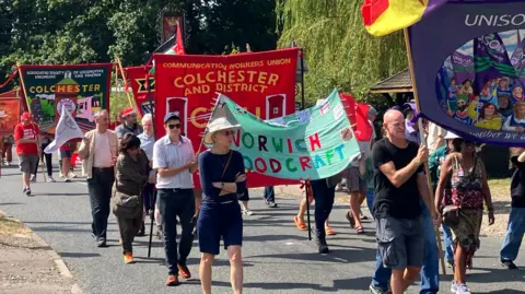 People hold up banners displaying their trade unions while walking down a road