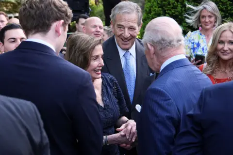 Julia Demaree Nikhinson / Pool via Reuters Nancy Pelosi in a blue dress chats with the King in a pinstripe suit at the garden party in the gardens of the British Embassy in Washington. Other guests watch on in the background.