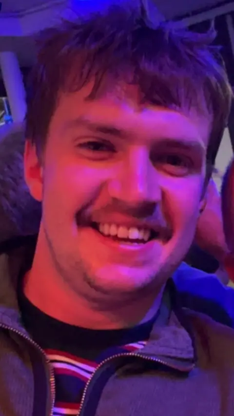 Rhodri Lewis A man smiles at the camera. He has short dark hair and a moustache.