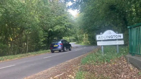 Photograph of a road on the edge of the village of Adlington, There is a car driving on a rural road from the village of Prestbury.
