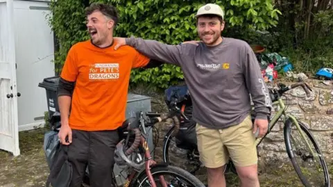 @devonbaistobyronbay Conrad (left) and Bobby with their hands on each others shoulders. They have biked behind them. They are both smiling.