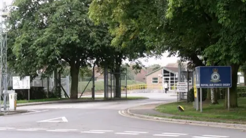 The entrance to RAF Digby, with trees and a road covering the building and a sign that says: "Royal Air Force Digby"