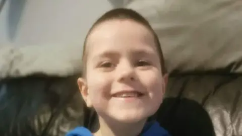 A close up image of a young boy, with short brown hair, smiling at the camera. 