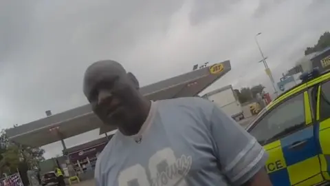 Northumbria Police A screenshot taken from a bodycam worn by PC Hunter. It shows Bellow standing in front of the officer. A police car is parked behind him and a Jet petrol station can be seen in the background.