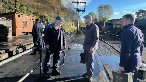 Half a dozen men, some wearing caps, are standing near or on the tracks.